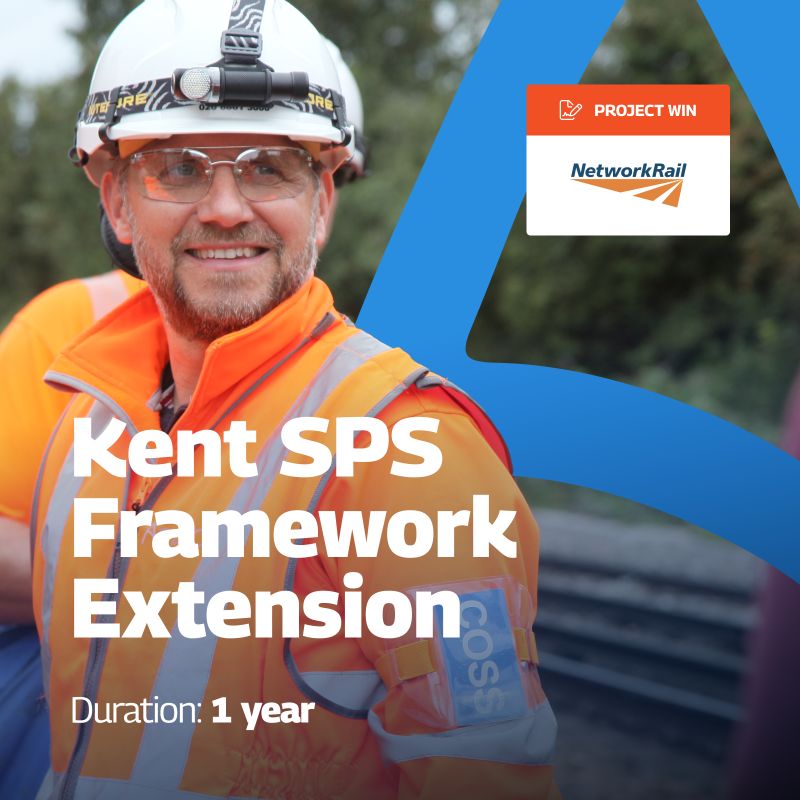 A promotional graphic announcing the Kent SPS Framework Extension project win with Network Rail. The image features a worker in high-visibility orange safety gear and a helmet, smiling while on-site. The text “Kent SPS Framework Extension” is prominently displayed in bold white letters, with “Duration: 1 year” noted below. In the top right corner, an orange label reads “PROJECT WIN” next to the Network Rail logo. The background includes a blue design element on the right side.