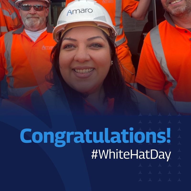 A celebratory graphic featuring a group of Amaro workers in high-visibility orange gear and safety helmets. The focus is on a smiling woman in the foreground wearing a white Amaro-branded helmet. The text “Congratulations! #WhiteHatDay” is prominently displayed in bold blue letters at the bottom of the image. The background includes additional team members in similar attire, contributing to a positive and celebratory atmosphere.