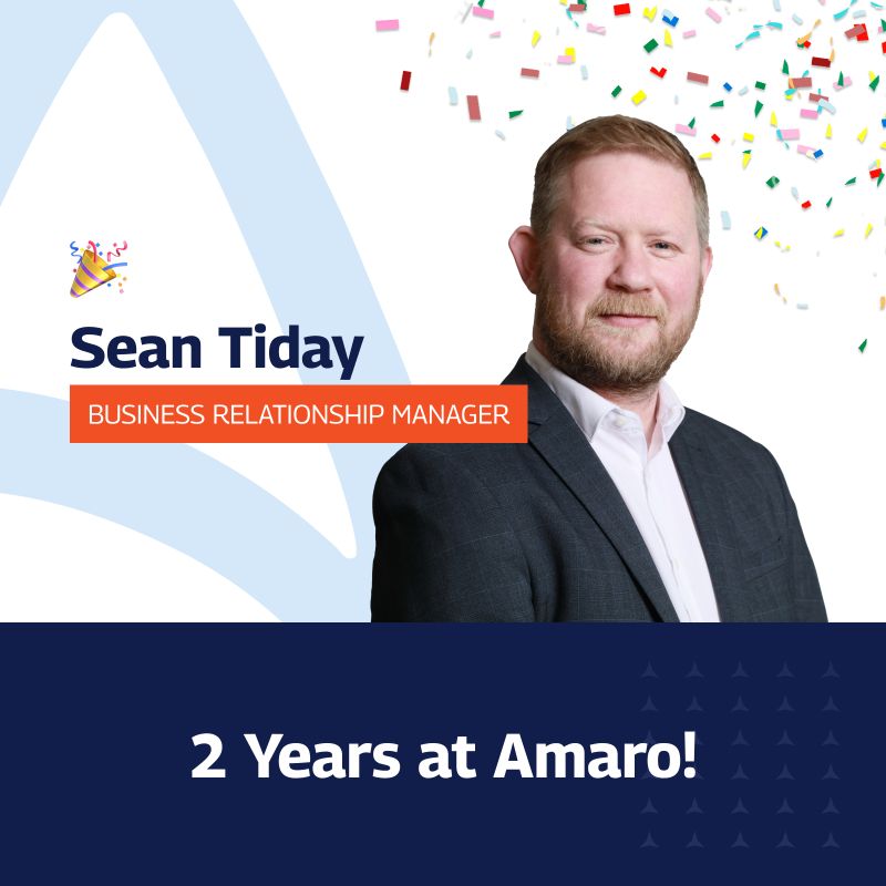 The image features a celebratory graphic for Sean Tiday, who is a Business Relationship Manager at Amaro. It commemorates his two-year anniversary with the company. The graphic includes a portrait of Sean, a Caucasian man with a beard, smiling and dressed in a business suit. The background is festive with confetti and features a large white triangle overlay. Text on the image states his name and job title, along with “2 Years at Amaro!” in bold lettering, all set against a blue and white colour scheme with star patterns on the bottom.